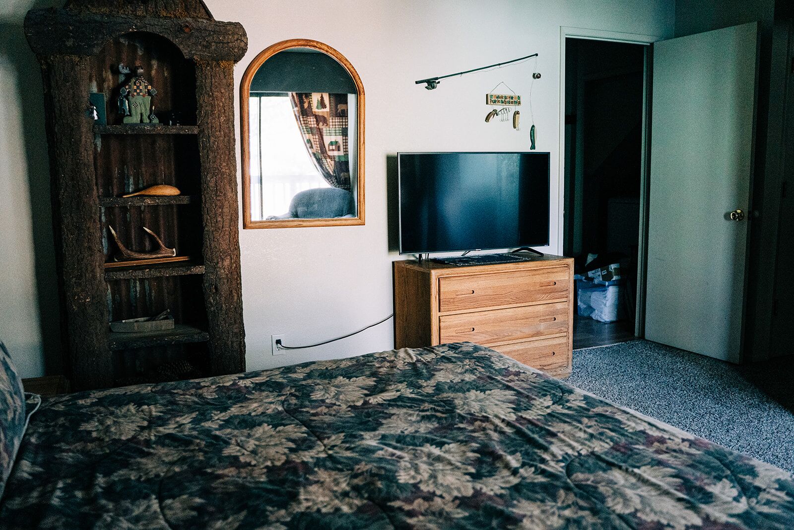 A bedroom with a bed, a dresser, a television, a mirror, and a shelf with various items.
