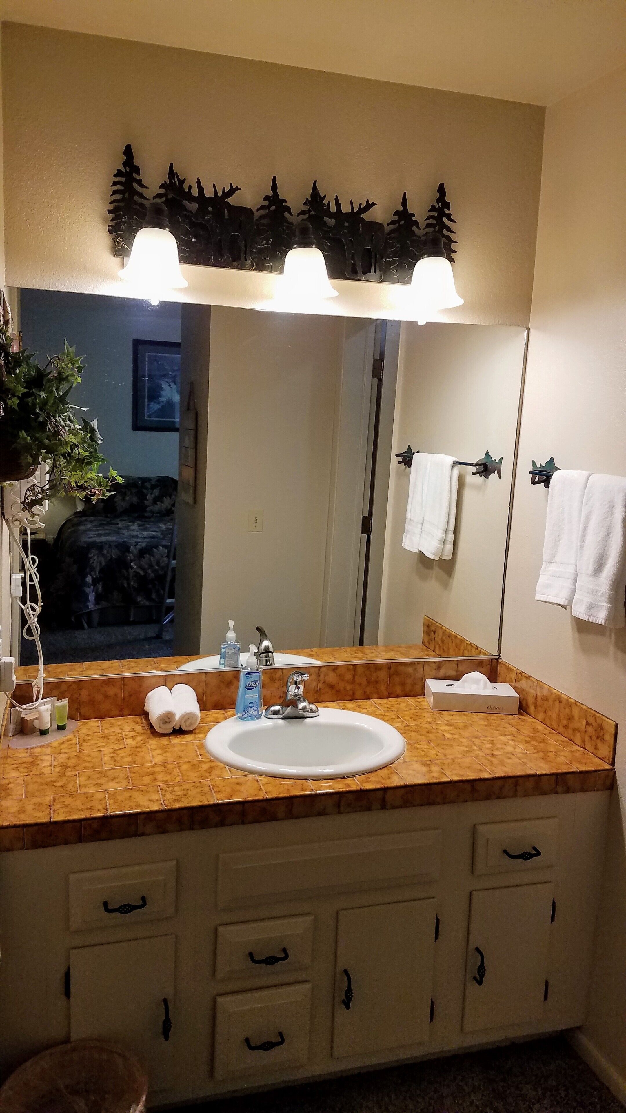 Een badkamer met een wastafel, spiegel, handdoekhouder en een decoratief kunstwerk boven de spiegel.