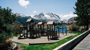 A playground with climbing structures and slides, surrounded by a grassy area and a view of snow-capped mountains. - June Lake Home with a view - 2bd / 2ba + loft (June Lake)