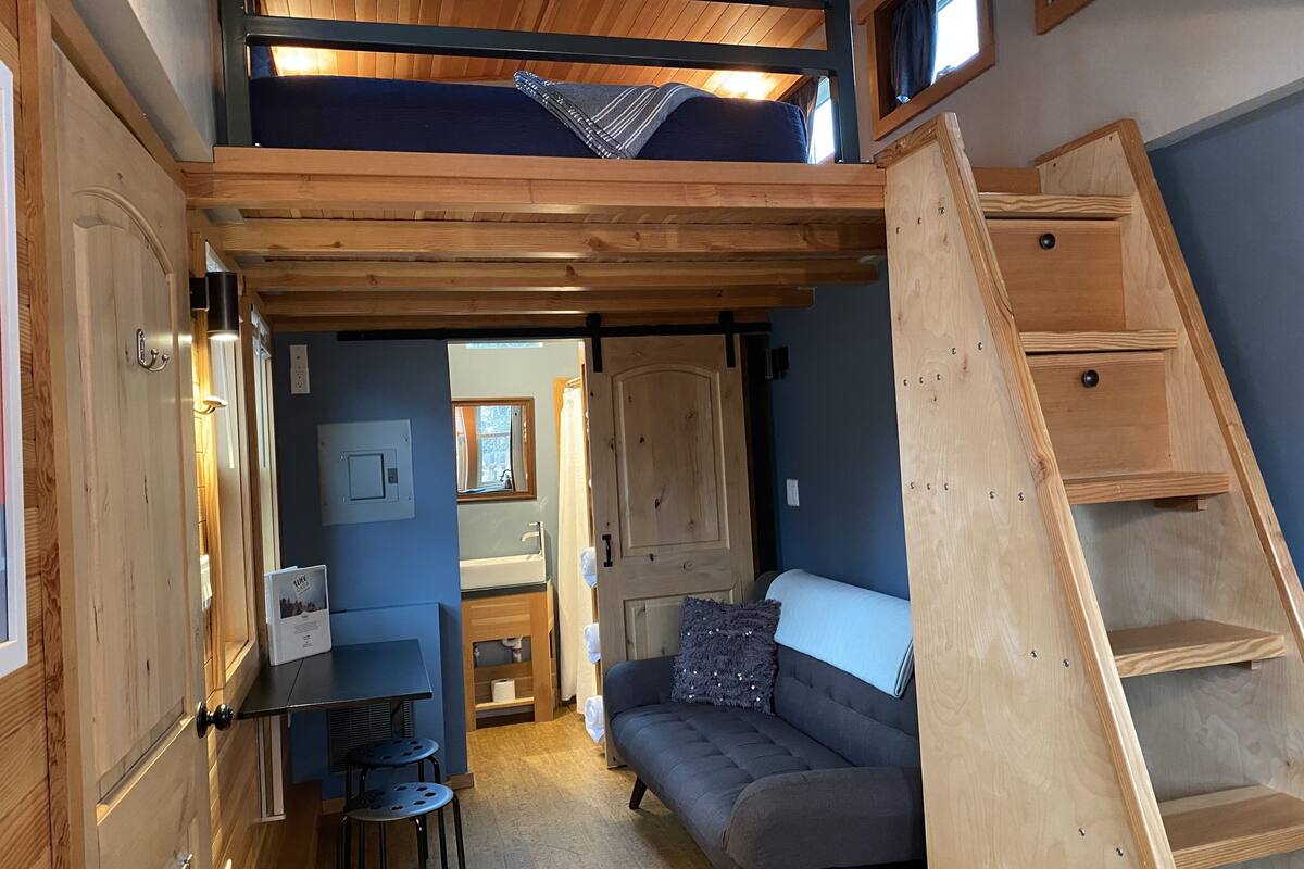 A compact living space with a bunk bed, a sofa, a small table, and a wooden ladder.