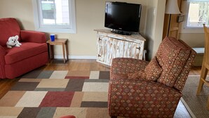 Una sala de estar con un sofá rojo, un sillón estampado, un televisor sobre un mueble de madera y un ventanal colorido.