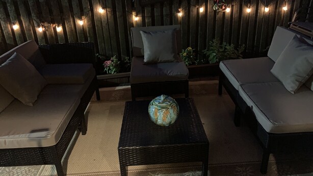Un área de estar al aire libre con dos sofás y una mesa de centro, rodeada por una valla de madera con luces colgantes.