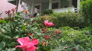 Una casa de dos pisos con un porche y un jardín lleno de flores rosadas.