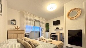 Un dormitorio moderno con cama, escritorio, silla, televisor y ventana con cortinas.
