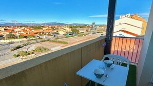 Un balcón con una mesa y sillas, con vistas a un paisaje urbano con edificios y un cielo despejado.