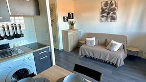 Una cocina moderna con lavadora integrada, un comedor con mesa de madera y individuales grises, y una sala de estar con sofá y arte decorativo en la pared.