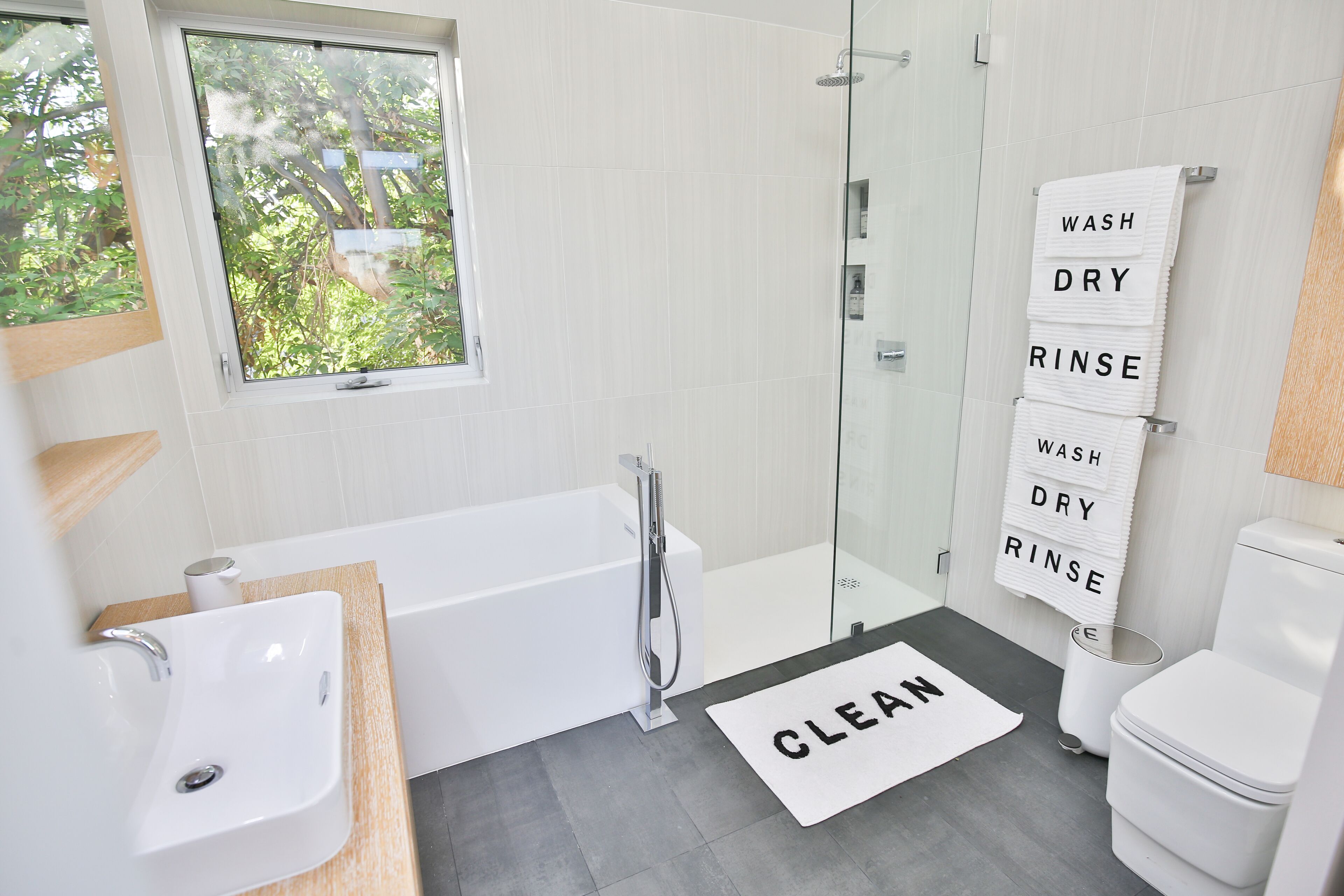 A modern bathroom with a bathtub, a shower, a toilet, and a window with a view of greenery.