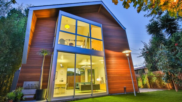 Ett modernt hus med ett stort glasfönster, en träfasad och en välskött gräsmatta.