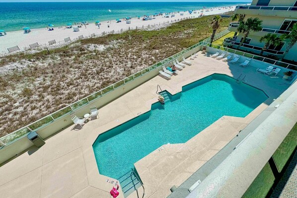 Une piscine avec vue sur une plage et un bâtiment doté d’un balcon.
