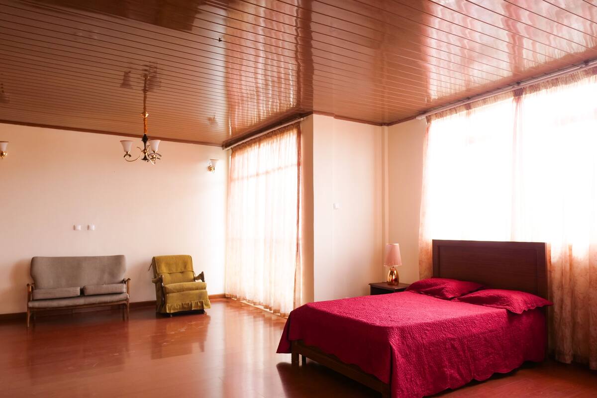 A spacious room with a large bed, two chairs, and a ceiling fan.