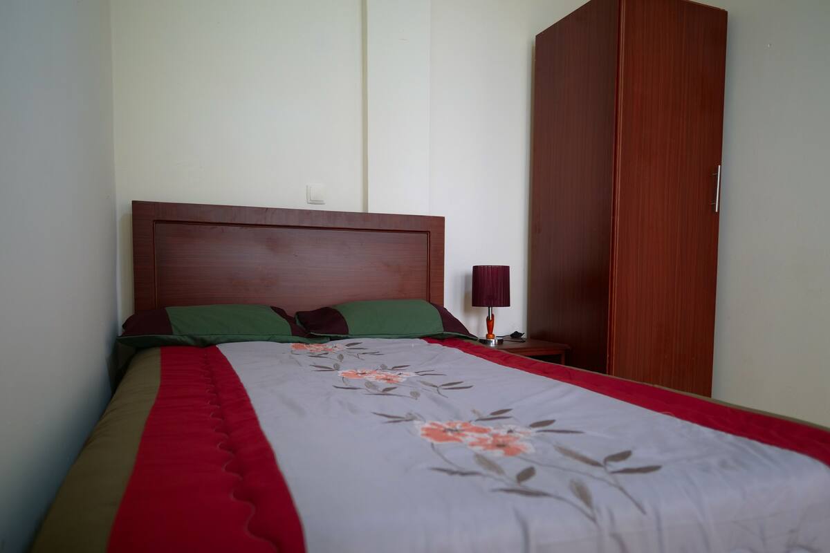 A neatly made bed with a floral bedspread, a wooden headboard, and a nightstand with a lamp.