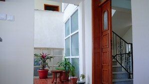 Un corridoio con una porta in legno, piante in vaso e una scala con ringhiere nere.