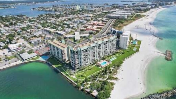An aerial view of a coastal city with a beachfront hotel, a marina, and a mix of residential and commercial buildings.