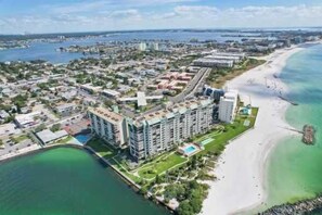 An aerial view of a coastal city with a beachfront hotel, a marina, and a mix of residential and commercial buildings. - 🌊 Gulf Winds #105 — Bright Beachside Studio with Balcony & Stunning Views (St Pete Beach)