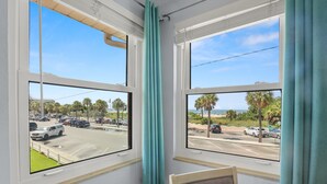 A room with two windows overlooking a parking lot and a beach.