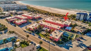 An aerial view of a coastal hotel area with multiple buildings, a beach, and a clear sky.