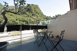 A balcony with a view of a river and hills, a table with chairs, and a potted plant. - Wulai Shui An Hot Spring House (New Taipei City)