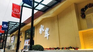 A building with a large illuminated sign, a covered entrance area, and a decorative wreath on the right. - Wulai Shui An Hot Spring House (New Taipei City)