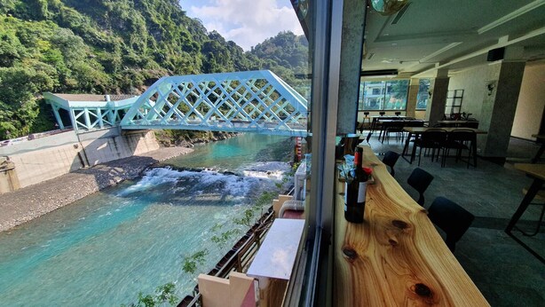 A view of a river with a bridge, a wooden table with a bottle, and a dining area with chairs and tables. - Wulai Shui An Hot Spring House (New Taipei City)