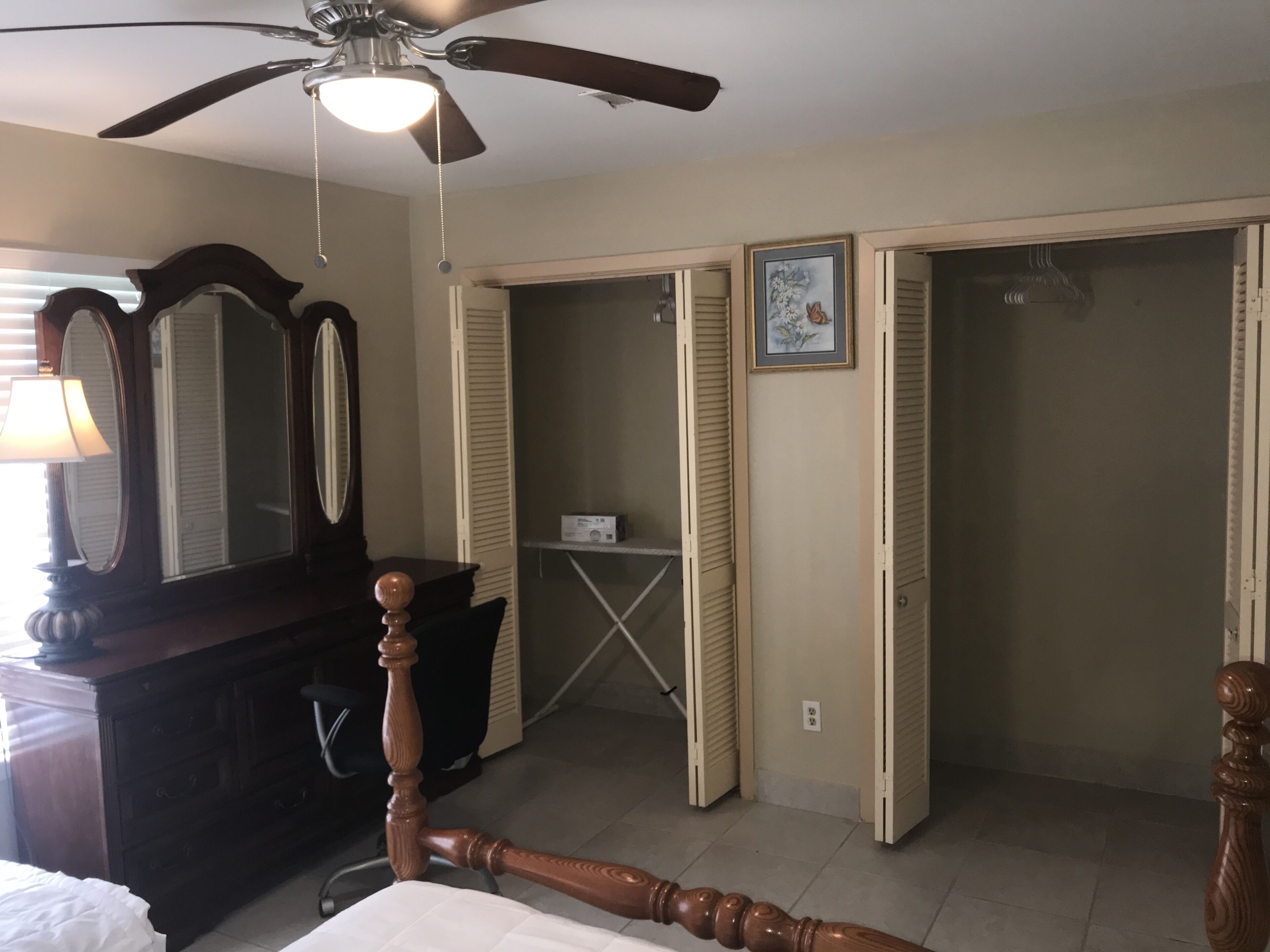 A bedroom with a bed, a dresser, a ceiling fan, a mirror, and a wardrobe.