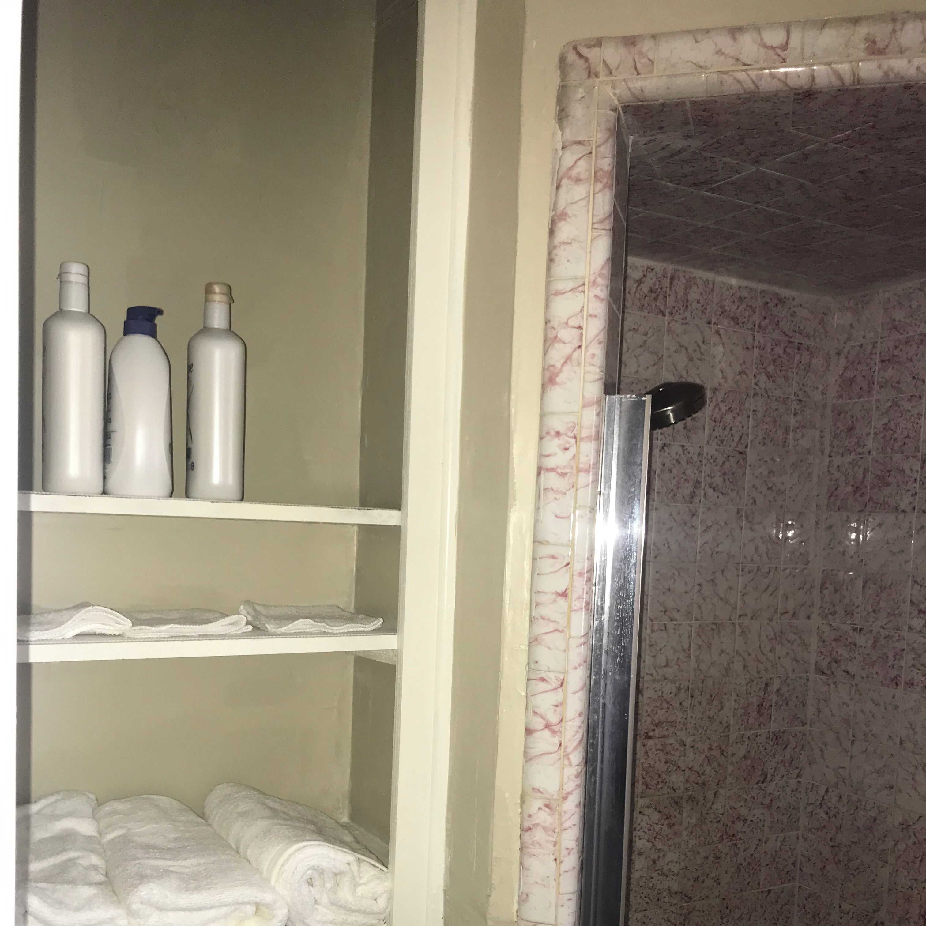 Et badeværelse med bruseniche i marmor, hvide hylder med toiletartikler og en håndklædestang.