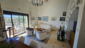 A spacious living room with a balcony, a white sofa, a coffee table, and a TV. - Villa with swimming pool and sea view over the bay of St-Tropez. Air conditioning. (LES ISSAMBRES)