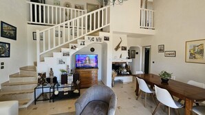 A spacious living area with a staircase, a dining table, and a television. - Villa with swimming pool and sea view over the bay of St-Tropez. Air conditioning. (LES ISSAMBRES)
