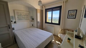 A bedroom with a bed, a window with a view, a desk with a chair, and a framed map on the wall. - Villa with swimming pool and sea view over the bay of St-Tropez. Air conditioning. (LES ISSAMBRES)