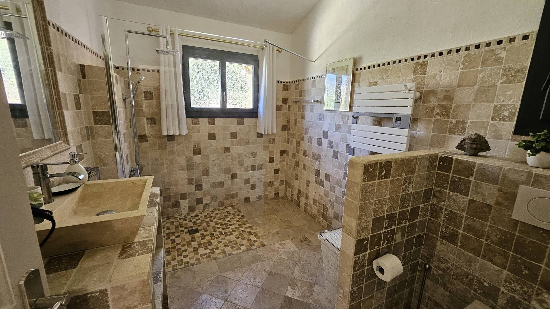 A bathroom with a shower, a sink, a window, and a toilet.