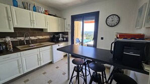 A kitchen with white cabinets, a black countertop, a sink, a dishwasher, and a window with a view. - Villa with swimming pool and sea view over the bay of St-Tropez. Air conditioning. (LES ISSAMBRES)