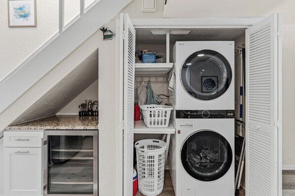 A laundry room with a stacked washer and dryer, a small cabinet, and a dish rack. - 1 Step to the Beach! Beachfront Condo with 3 Sunset Decks, Sleeps 6 (Indian Rocks Beach)