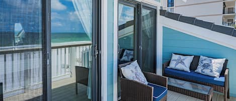 A balcony with a wicker chair and cushions, a glass door, and a view of the ocean.
