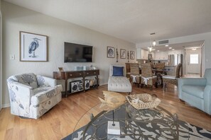 A living room with a sofa, a coffee table, and a television. There is a kitchen area with a dining table and chairs. - 1 step and you are on the BEACH! Watch amazing sunsets from 3 decks! PremierHost (Indian Rocks Beach)