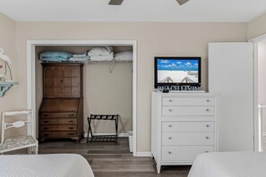 Ein Schlafzimmer mit einem Bett, einem Kleiderschrank, einem Schminktisch und einem Fernseher, der eine Strandansicht zeigt.