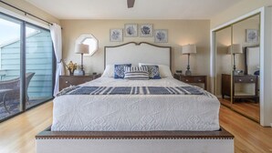 A bedroom with a large bed, a ceiling fan, a sliding glass door to a balcony, and a mirror. - 1 step and you are on the BEACH! Watch amazing sunsets from 3 decks! PremierHost (Indian Rocks Beach)