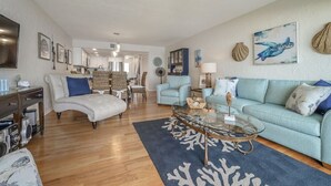 A spacious living room with a light blue sofa, a glass coffee table, and a blue rug. - 1 step and you are on the BEACH! Watch amazing sunsets from 3 decks! PremierHost (Indian Rocks Beach)