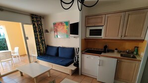 Un espacio habitable compacto con sofá, mesa de comedor, kitchenette y vistas al exterior.