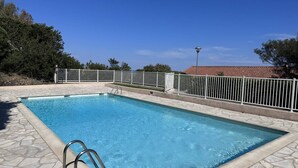 Une piscine rectangulaire avec un escalier en métal, entourée d’une terrasse en pierre et d’une clôture en métal blanc.