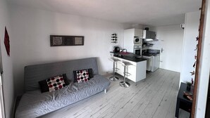 Un espace de vie compact comprenant un canapé gris, une kitchenette et un petit coin repas.