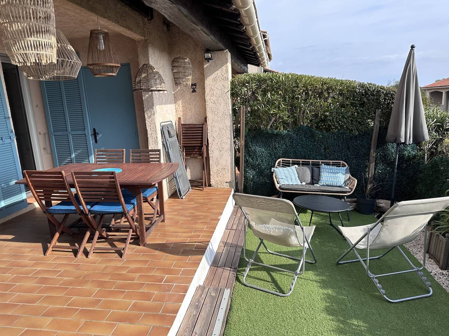 Eine Terrasse im Freien mit einem Holztisch und -stühlen, einer gepolsterten Couch und einem kleinen runden Tisch.
