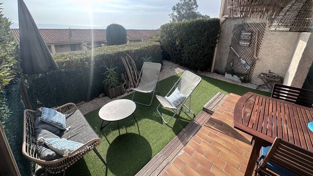 Un espace patio aménagé avec une table en bois, deux chaises, une petite table ronde et un fauteuil en osier avec des coussins.