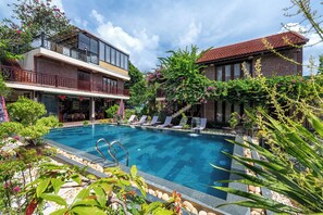 A swimming pool with lounge chairs, surrounded by greenery and a building with a balcony. - Tamcoc Ngoc Linh Homestay (Nam Hoa Lu)