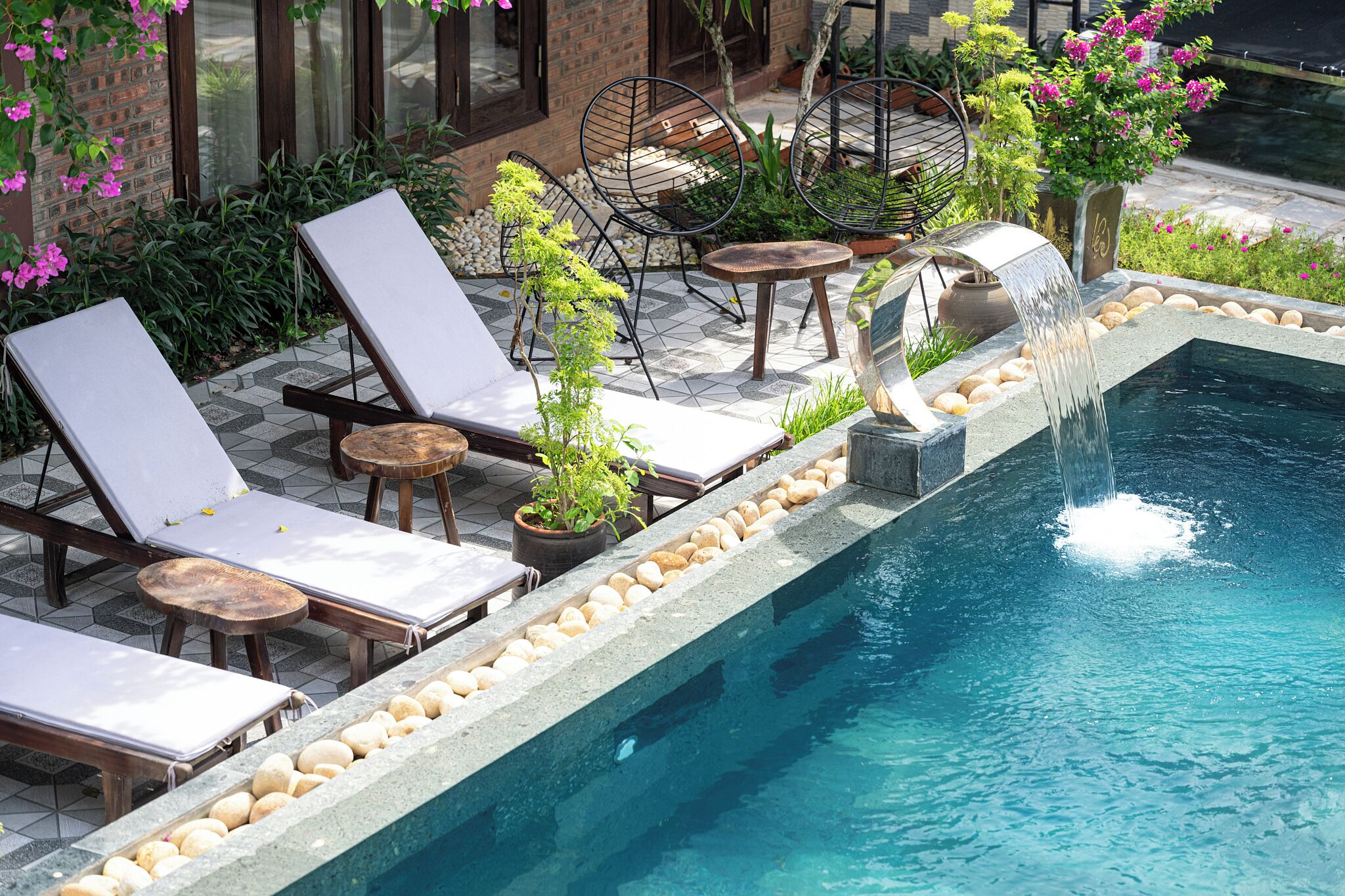 A poolside area with lounge chairs, a small table, and a decorative fountain.