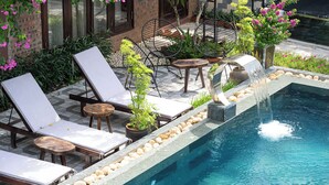 A poolside area with lounge chairs, a small table, and a decorative fountain. - Tamcoc Ngoc Linh Homestay (Nam Hoa Lu)