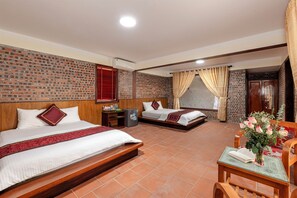 A hotel room with two beds, a small table with a vase of flowers, a desk with a computer, and a brick wall. - Tamcoc Ngoc Linh Homestay (Hoa Lu)