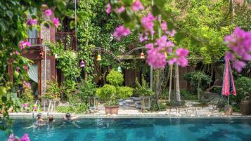 Una piscina con gente nadando, rodeada de exuberante follaje y plantas en macetas.