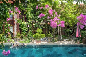 A swimming pool with people in the water, surrounded by lush greenery and potted plants. - Tamcoc Ngoc Linh Homestay (Nam Hoa Lu)