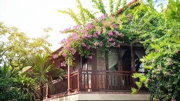 A two-story building with a balcony, surrounded by lush greenery and flowering plants.