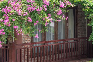 A balcony with a wooden railing, covered in pink flowers, and a brick wall in the background. - Tamcoc Ngoc Linh Homestay (Nam Hoa Lu)