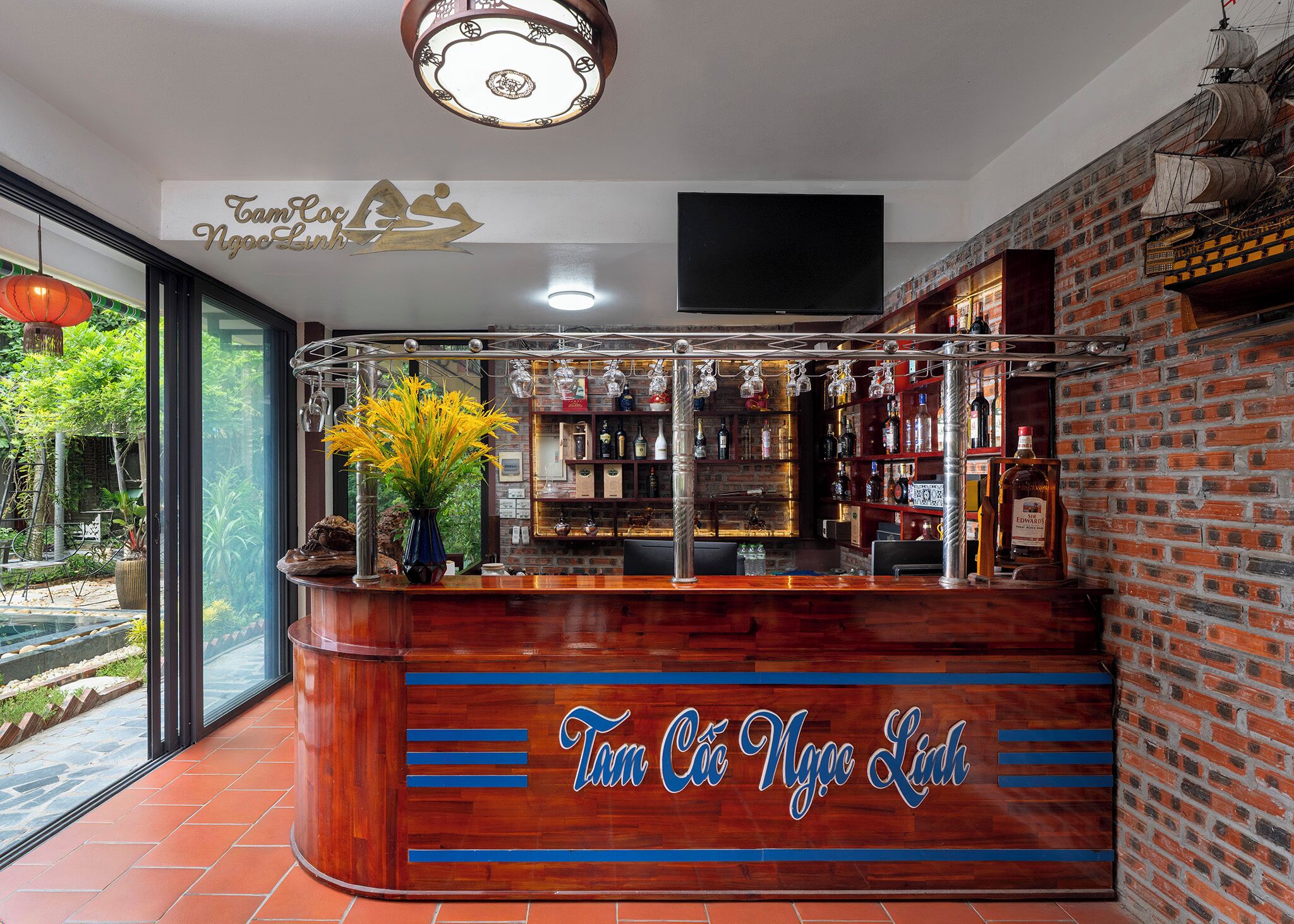 A bar area with a wooden counter, shelves with bottles, and a decorative hanging light fixture.
